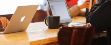 people sitting at a table working on their laptops and drinking coffee.