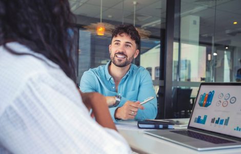 Man speaking to a woman with a computer showing charts