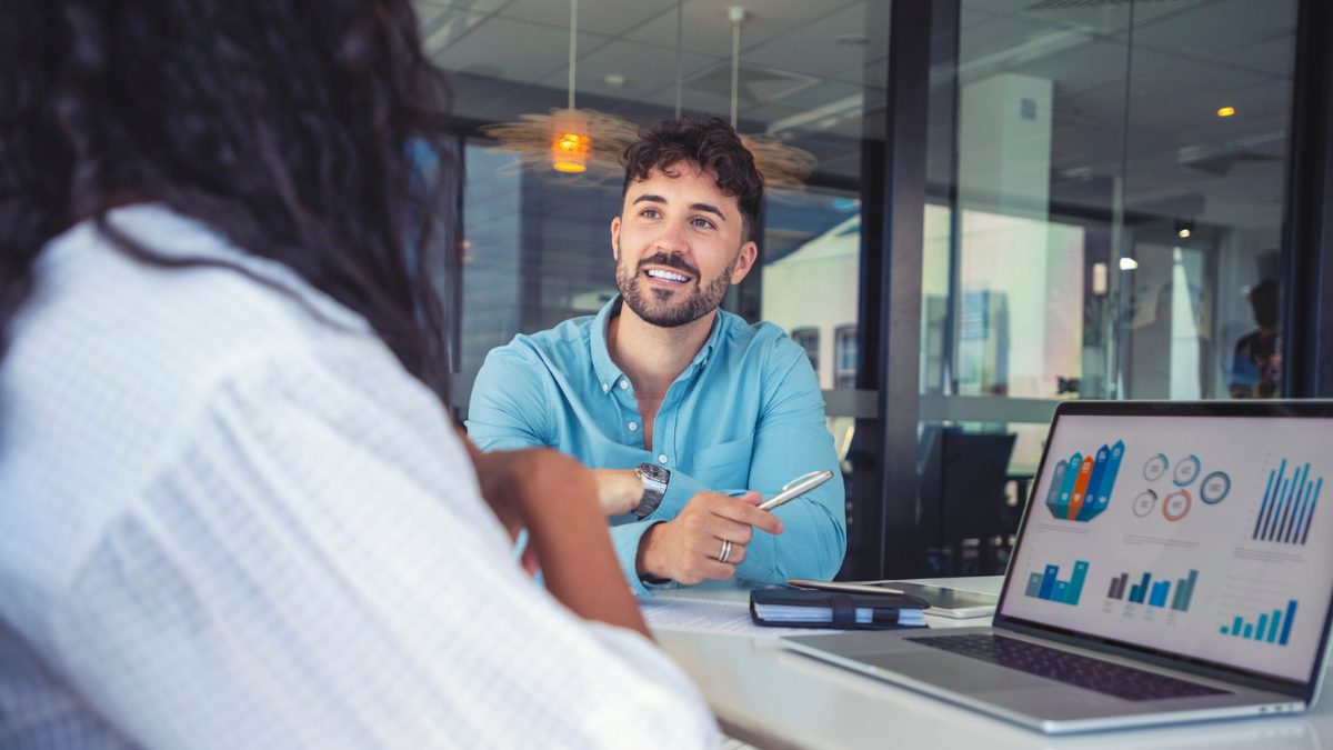 Man speaking to a woman with a computer showing charts